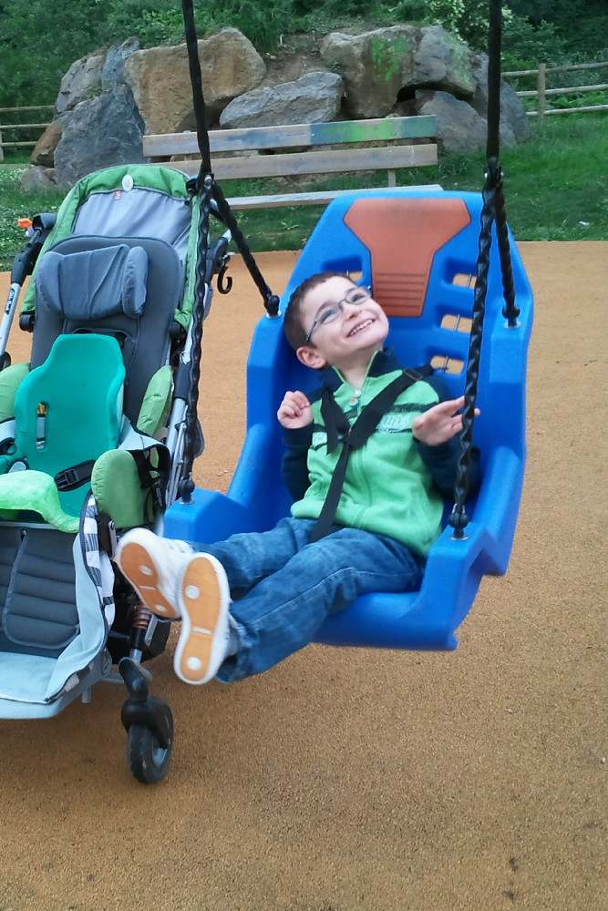 Child using an adaptive playground swing seat with supportive harness designed for inclusive play and accessibility.
